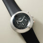 Ikepod Chronopod chronograph watch with silver case, black dial, and black leather strap on cream background.