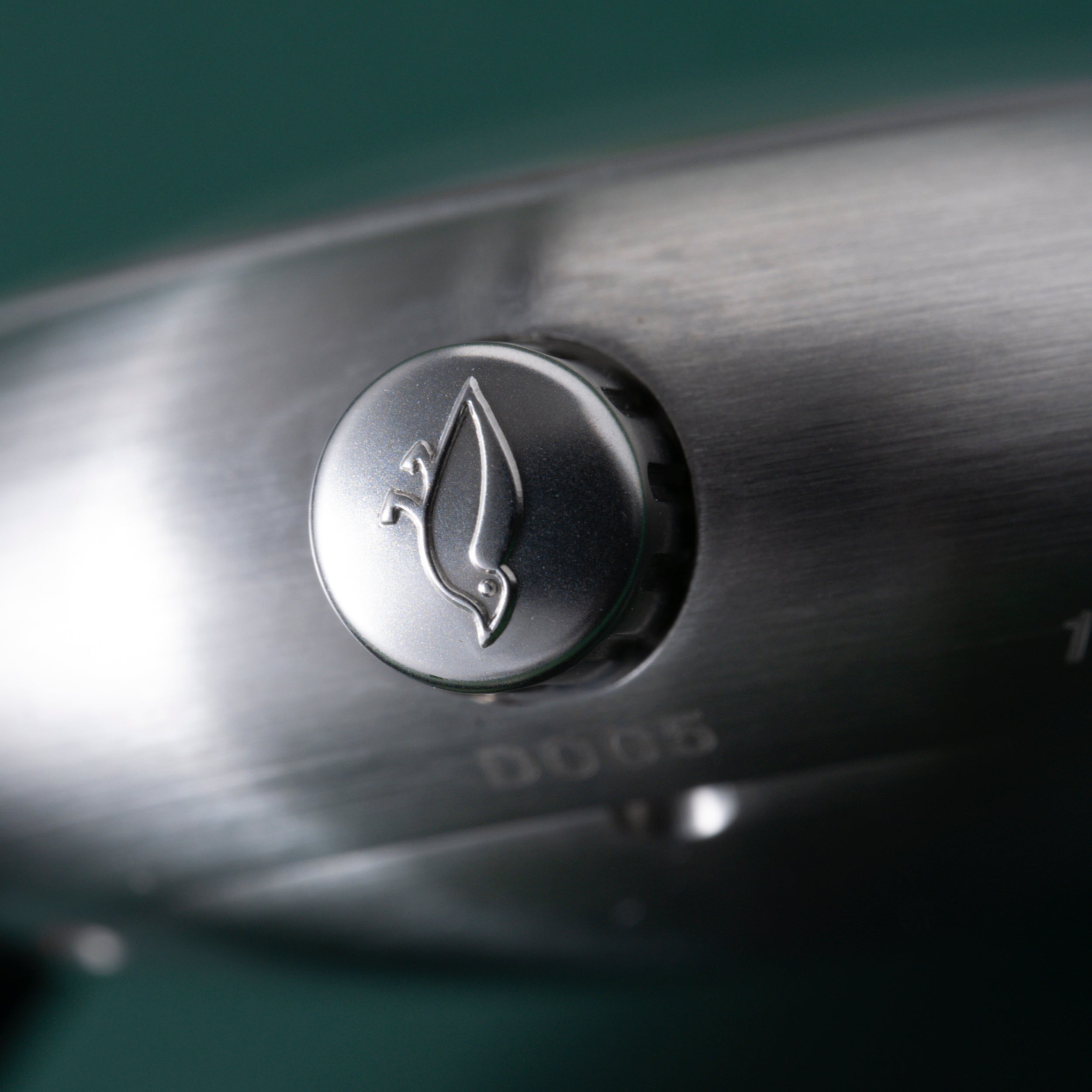 Silver-toned watch crown with leaf engraving on brushed metal watch case.