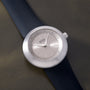White Ikepod Duopod watch with silver dial, hour markers, and hands on dark blue rubber strap.