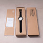 Ikepod Duopod watch with black strap and white dial displayed in cardboard packaging with documentation.