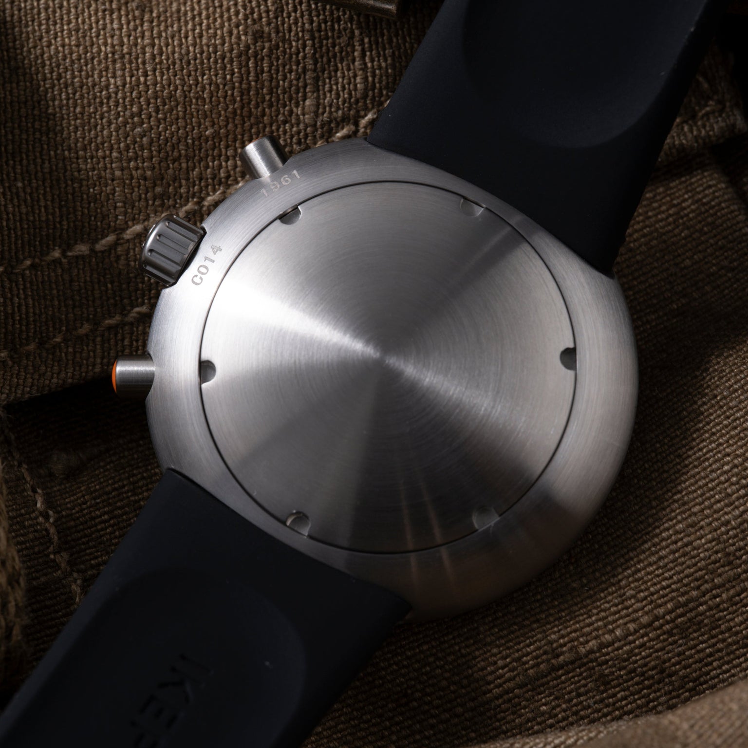 Ikepod Chronopod 'Hey Joe' 014 watch with brushed steel case, black strap, and orange accent on black textile background.