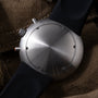 Ikepod Chronopod 'Hey Joe' 014 watch with brushed steel case, black strap, and orange accent on black textile background.