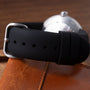 Two-pod watch with black rubber strap featuring gold dots and silver-tone case on brown leather surface.