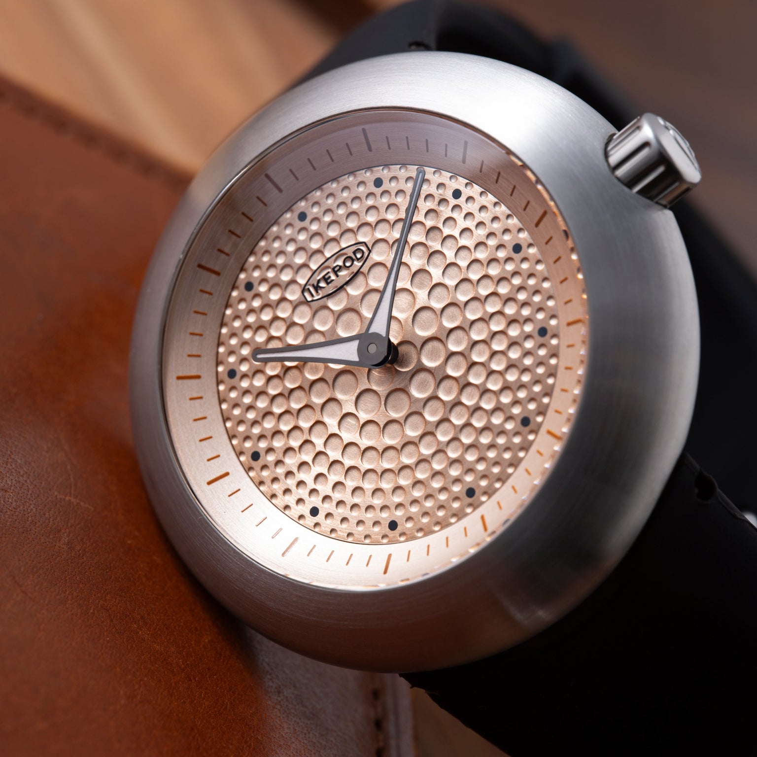 Ikepod Duopod watch with gold-tone textured dial, black hands, index markers, and silver case on brown leather strap.