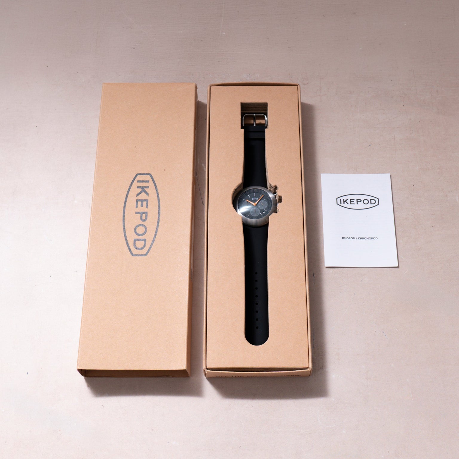 Ikepod Chronopod watch with black leather strap and blue dial in tan cardboard box with documentation.