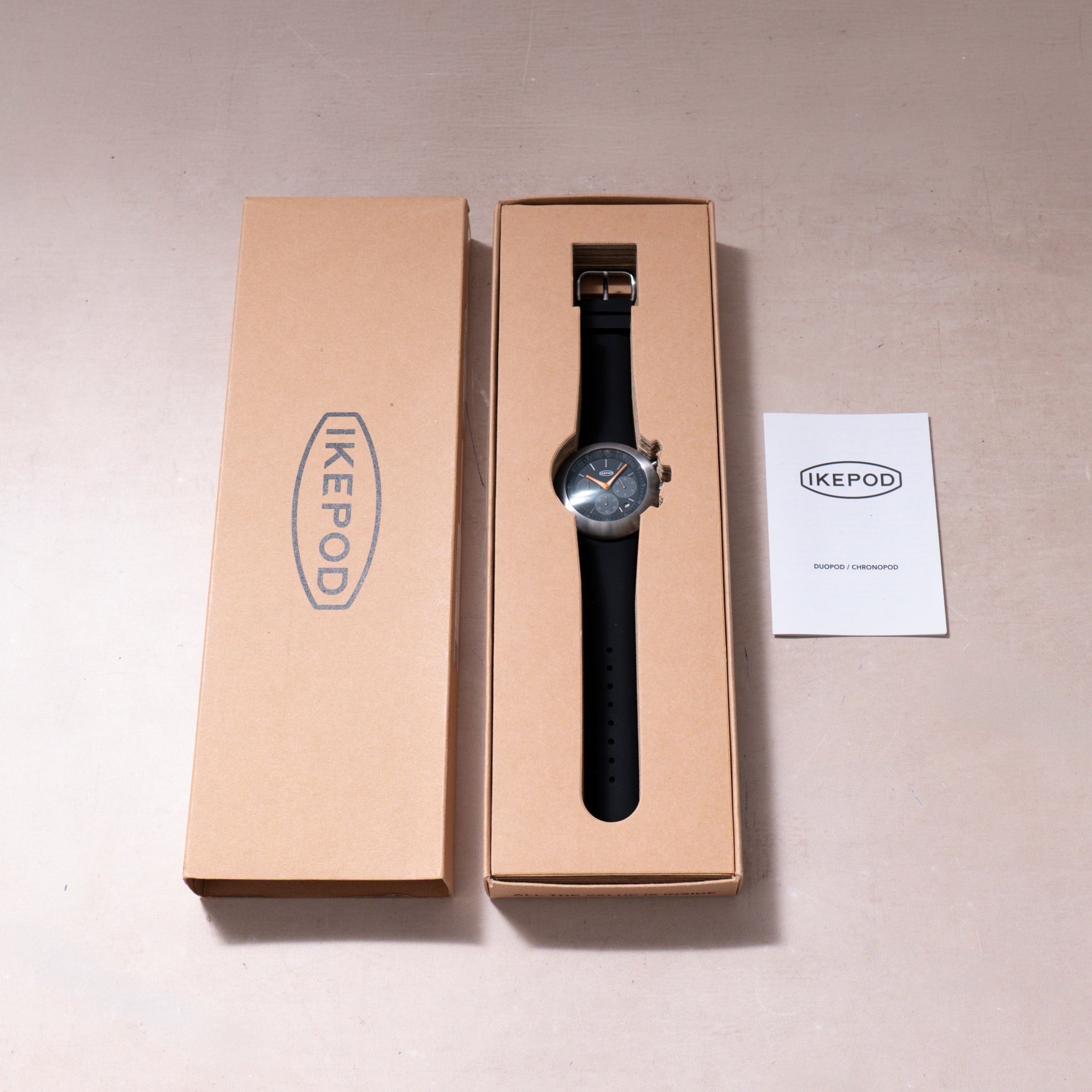 Ikepod Chronopod watch with black leather strap and blue dial in tan cardboard box with documentation.