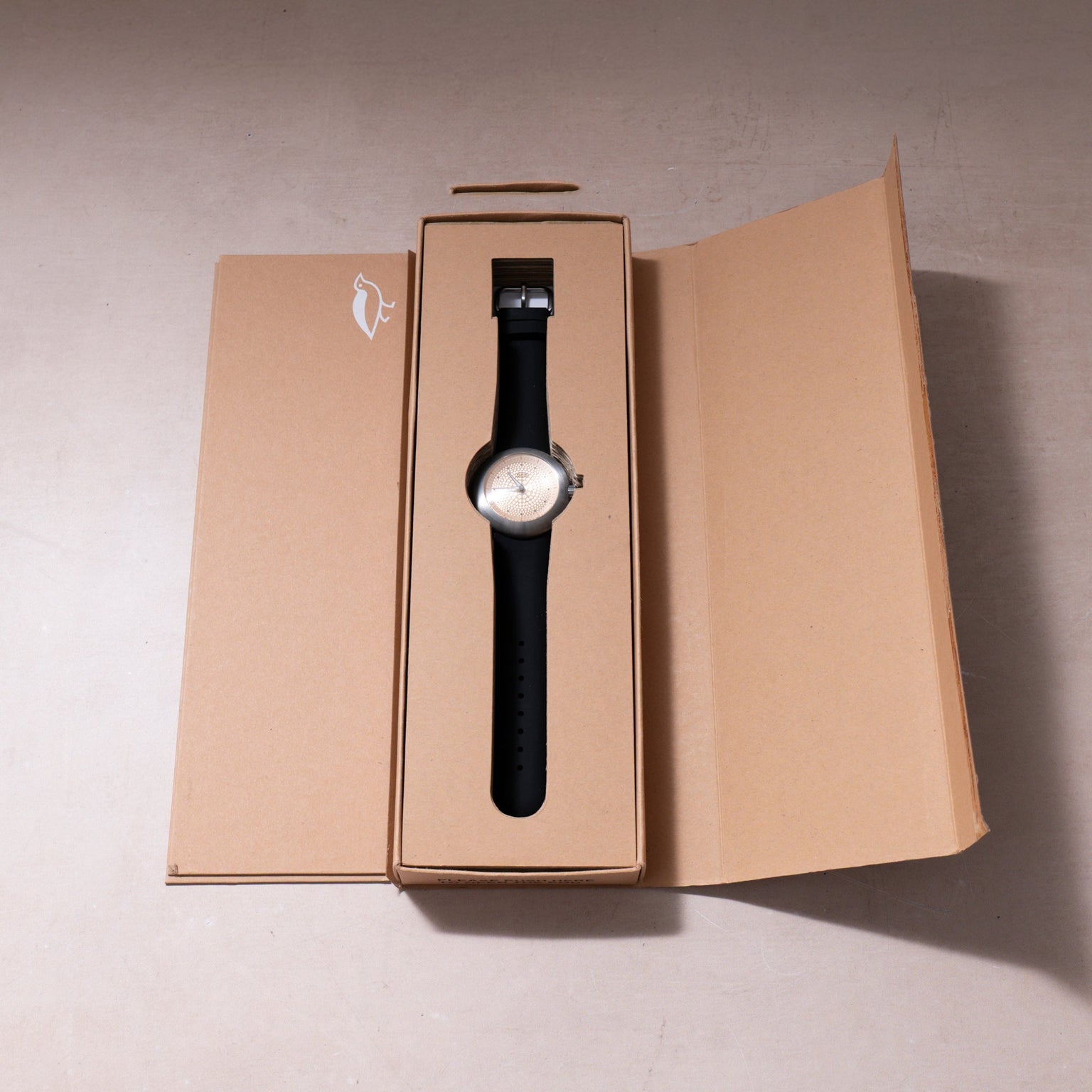 Ikepod Duopod watch with white dial and gold dots on black leather strap in open tan packaging box.