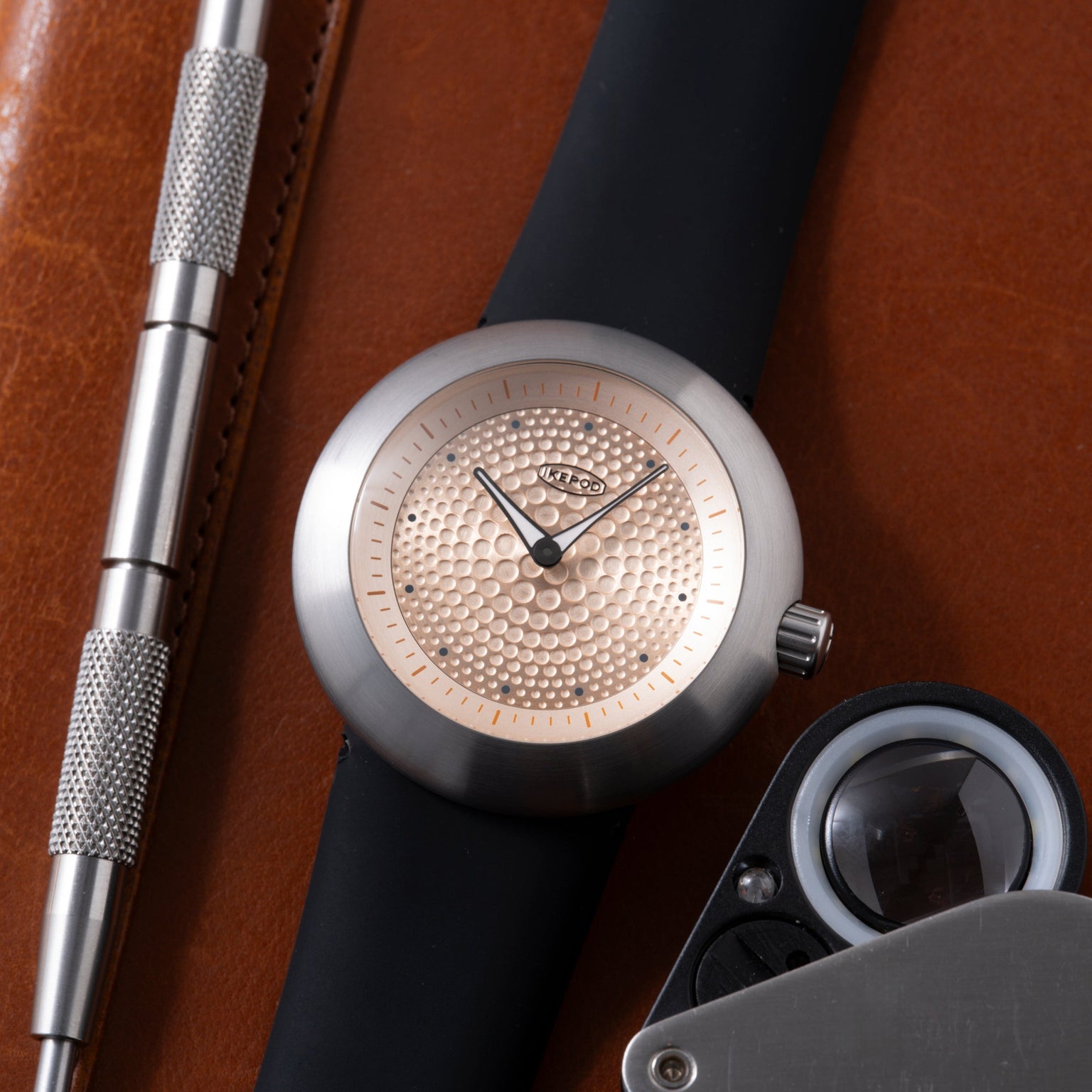 Silver watch with champagne dial featuring small dots pattern, black strap, and black hands on brown leather background.