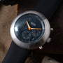 Ikepod Chronopod watch with brushed steel case, black dial, orange hands, and chronograph subdials on dark blue strap.