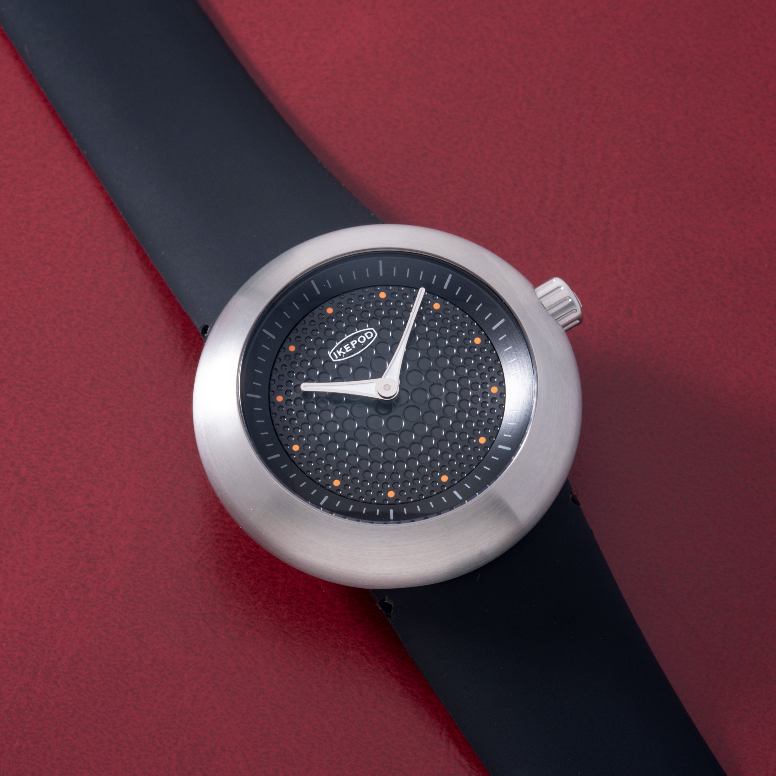Ikepod Duopod Dots 004 watch with silver case, black dial featuring orange dot markers, and black rubber strap.