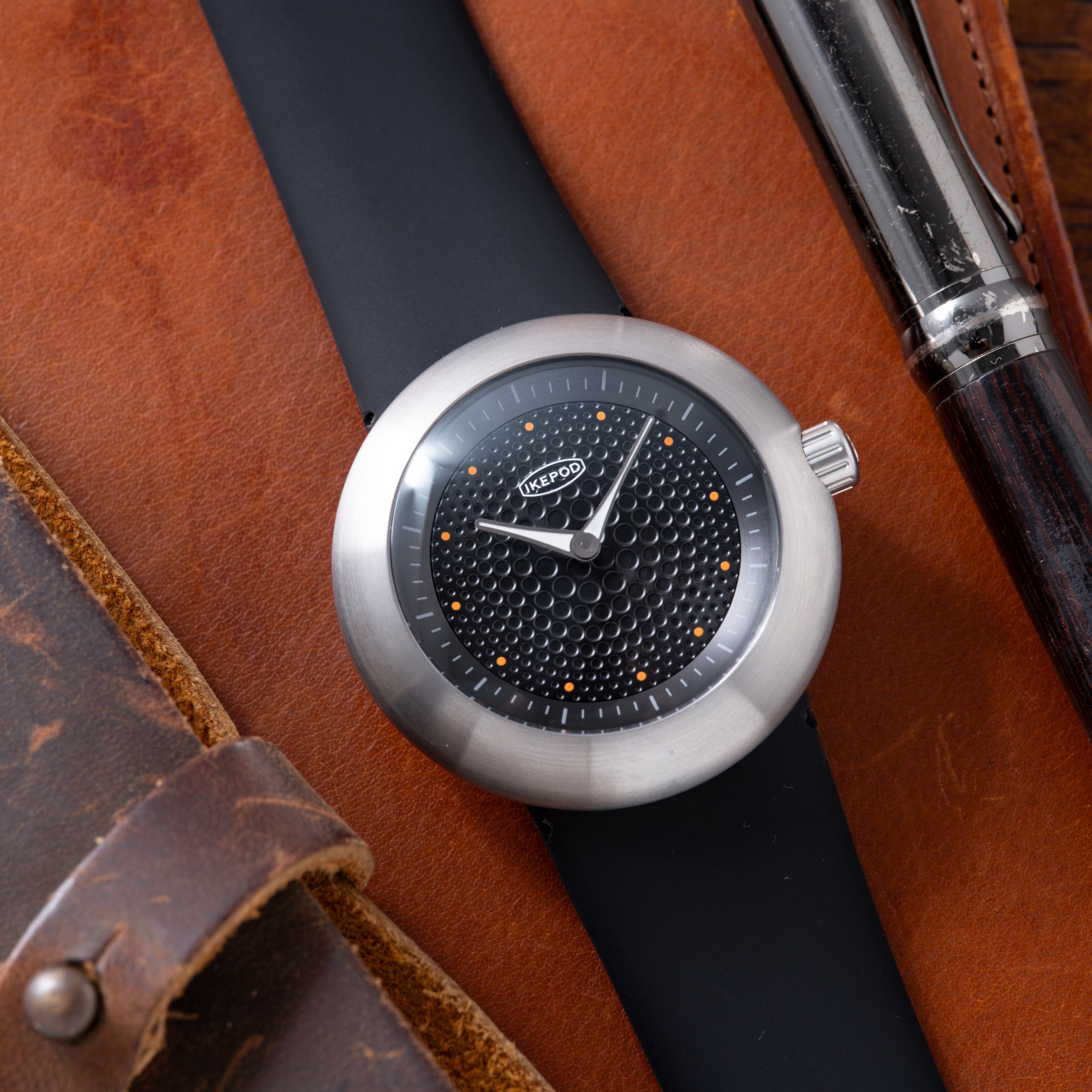 Ikepod Duopod watch with silver case, black dial featuring dot pattern, orange dot indices, and black leather strap.