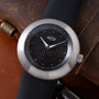 Ikepod Duopod watch with brushed steel case, black dial featuring orange dot hour markers, and dark rubber strap.