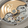 Close-up of exposed watch movement with polished steel plates, golden gears, ruby jewels, and engraved Patek Philippe logo.