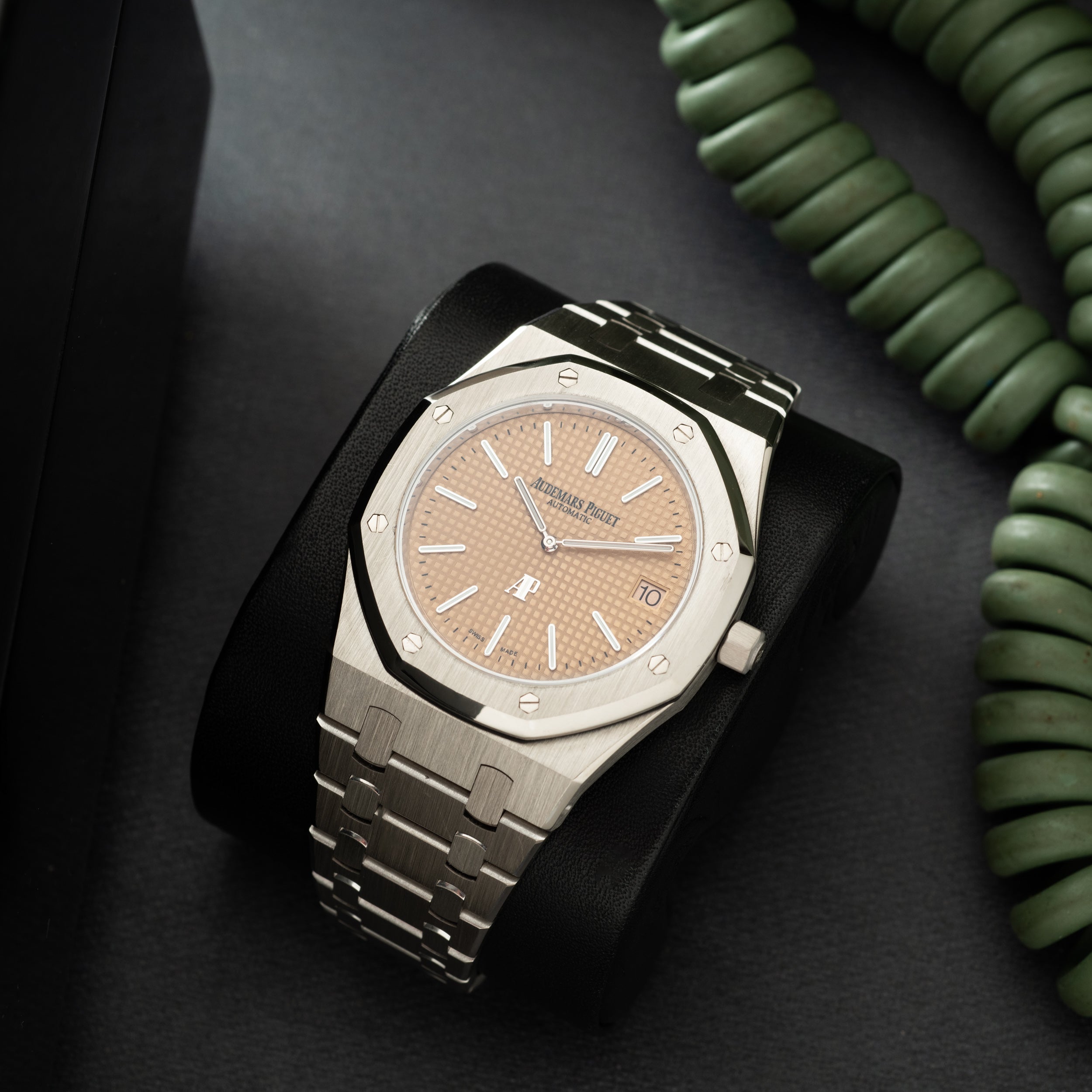 Stainless steel watch with octagonal bezel, salmon-colored dial, applied indices, and matching bracelet on black fabric.