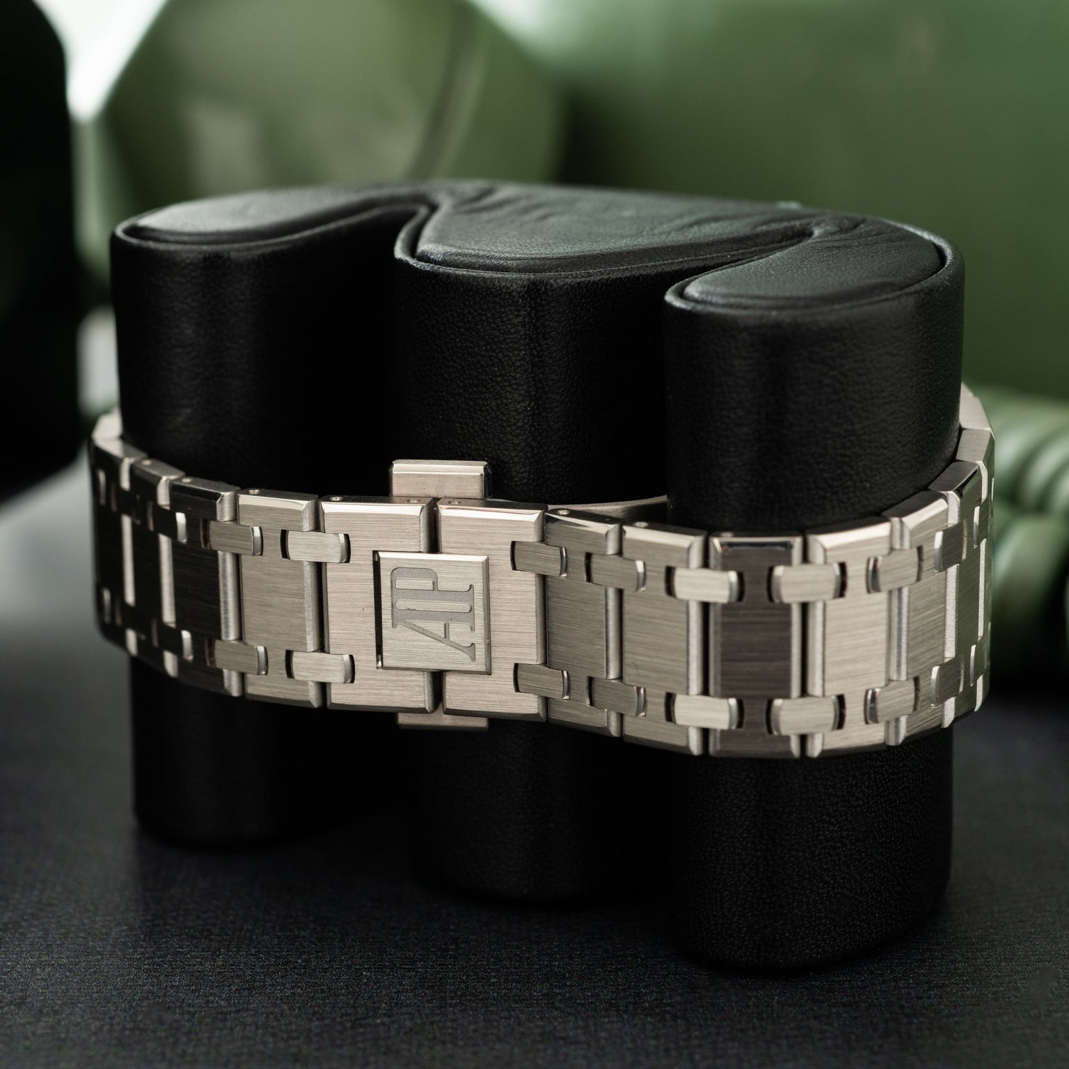 Stainless steel watch bracelet with integrated links and rectangular clasp displayed on black fabric rolls.