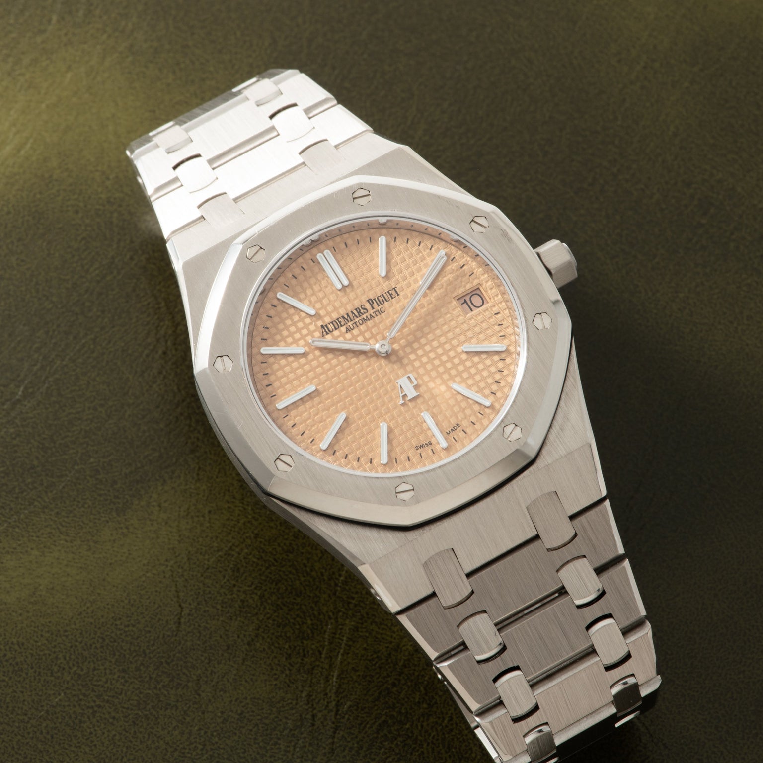 Stainless steel watch with octagonal bezel, salmon-colored dial, and matching bracelet on olive background.