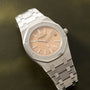 Stainless steel watch with octagonal bezel, salmon-colored dial, and matching bracelet on olive background.