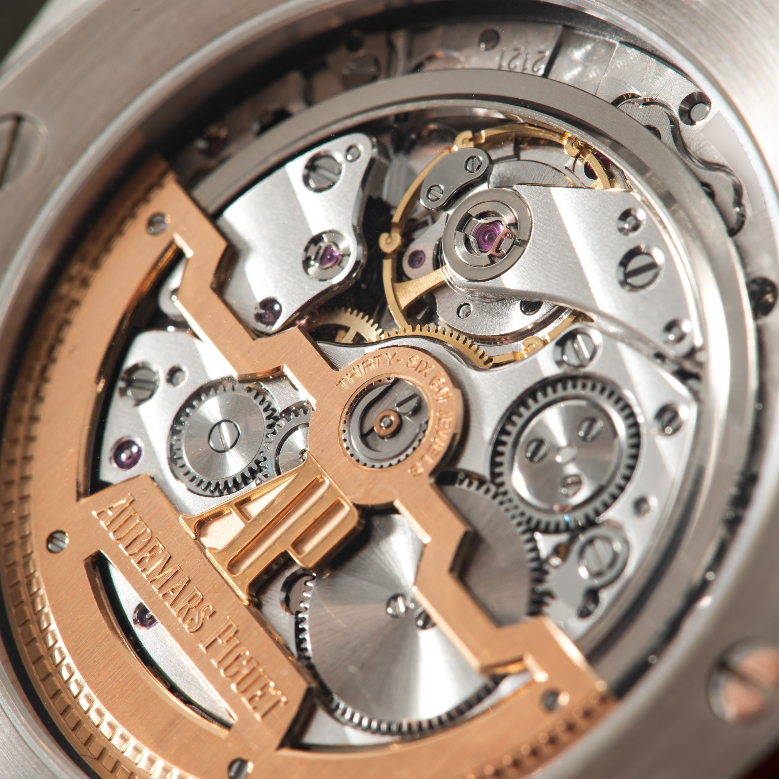 Exposed automatic watch movement with rose gold and steel components, gears, and jeweled bearings visible through caseback.