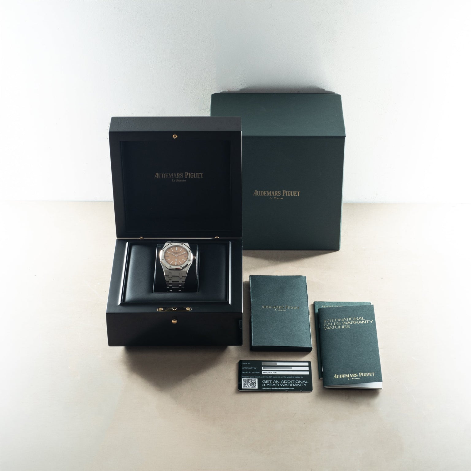 Audemars Piguet Royal Oak watch with salmon dial displayed in open black box with outer green packaging and documentation car