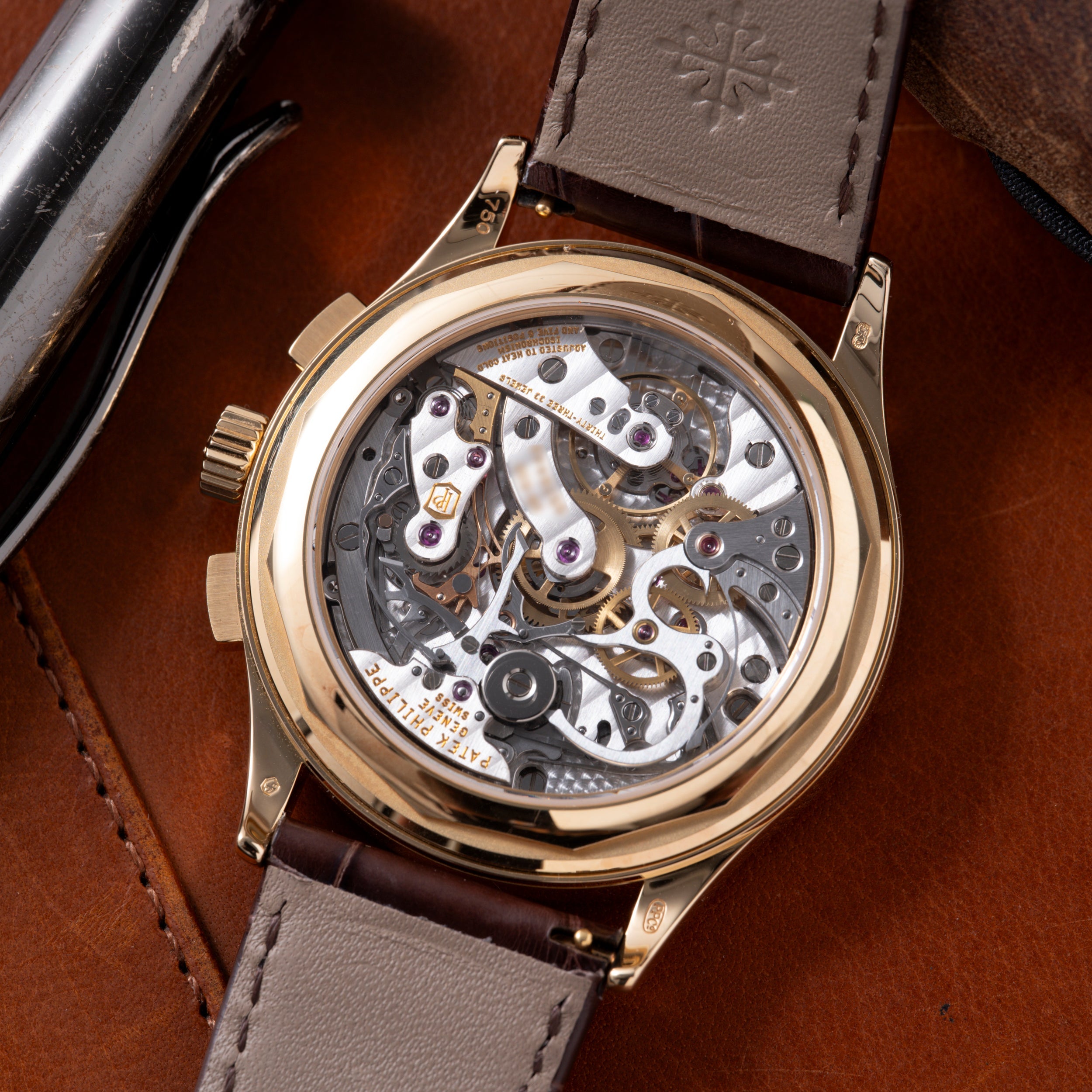 Gold-tone chronograph watch with exposed skeletal movement, white and black dial components, gray leather strap on brown back