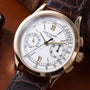 Patek Philippe chronograph watch with white dial, Roman numerals, subdials, and brown leather strap.