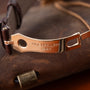 Gold-tone watch bracelet with "Patek Philippe Geneve" engraving and brown leather strap on fabric surface.