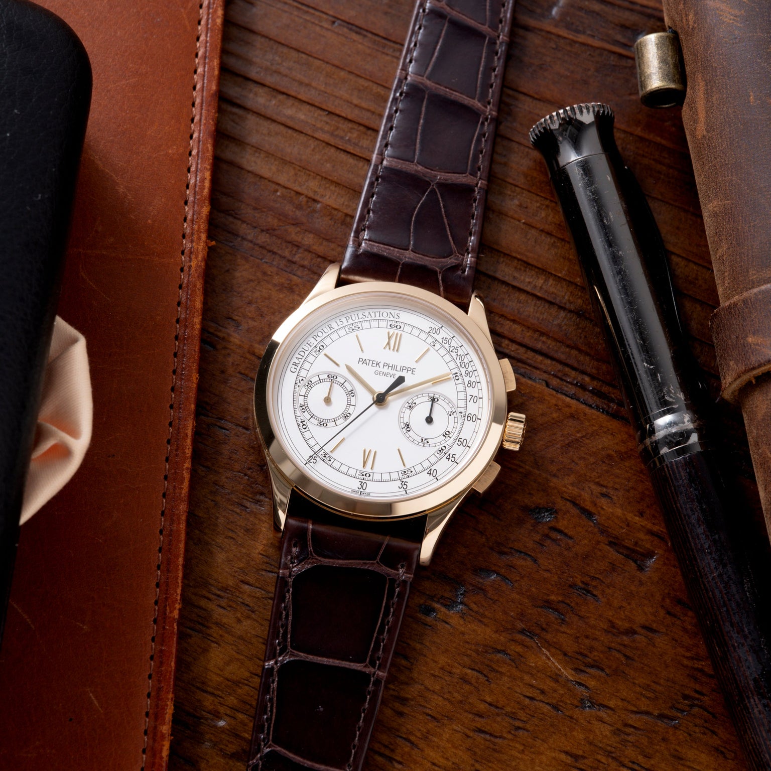 Patek Philippe chronograph with white dial, two subdials, and dark crocodile leather strap on wooden surface.