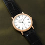 Gold-tone watch with white dial, Roman numerals, small subdial, and black crocodile leather strap.
