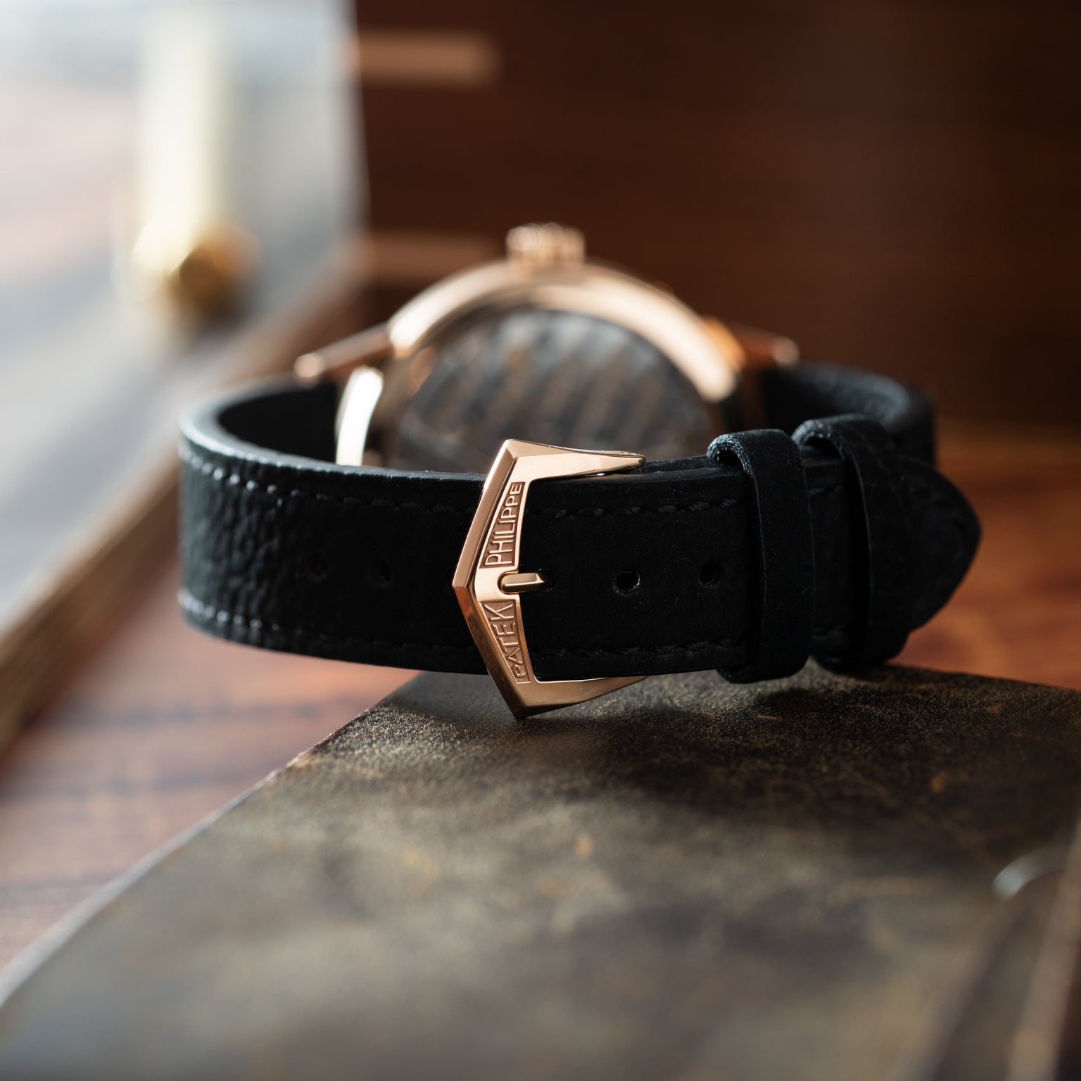 Rose gold watch with regulator dial and black leather strap on wooden surface.