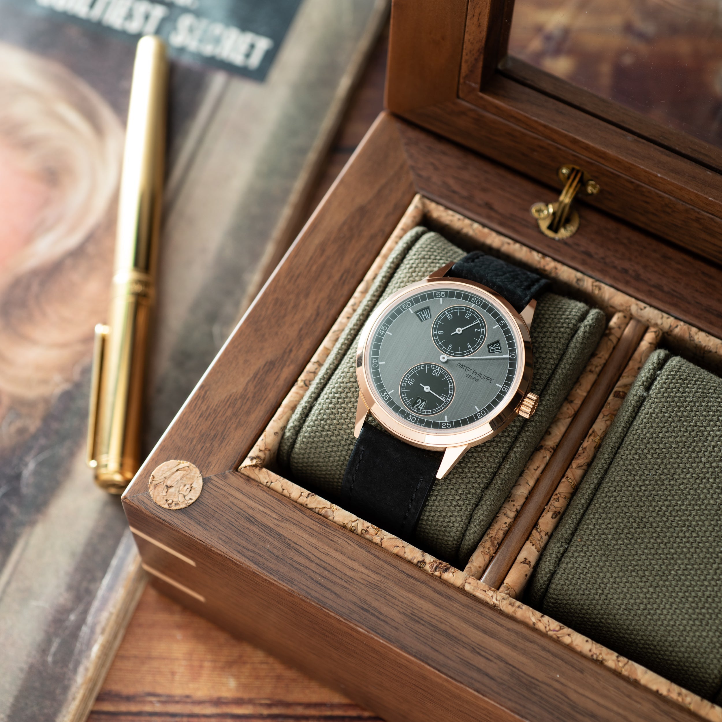 Silver-tone watch with dual subdials and olive green fabric strap displayed in wooden box with tan interior and brass hardwar