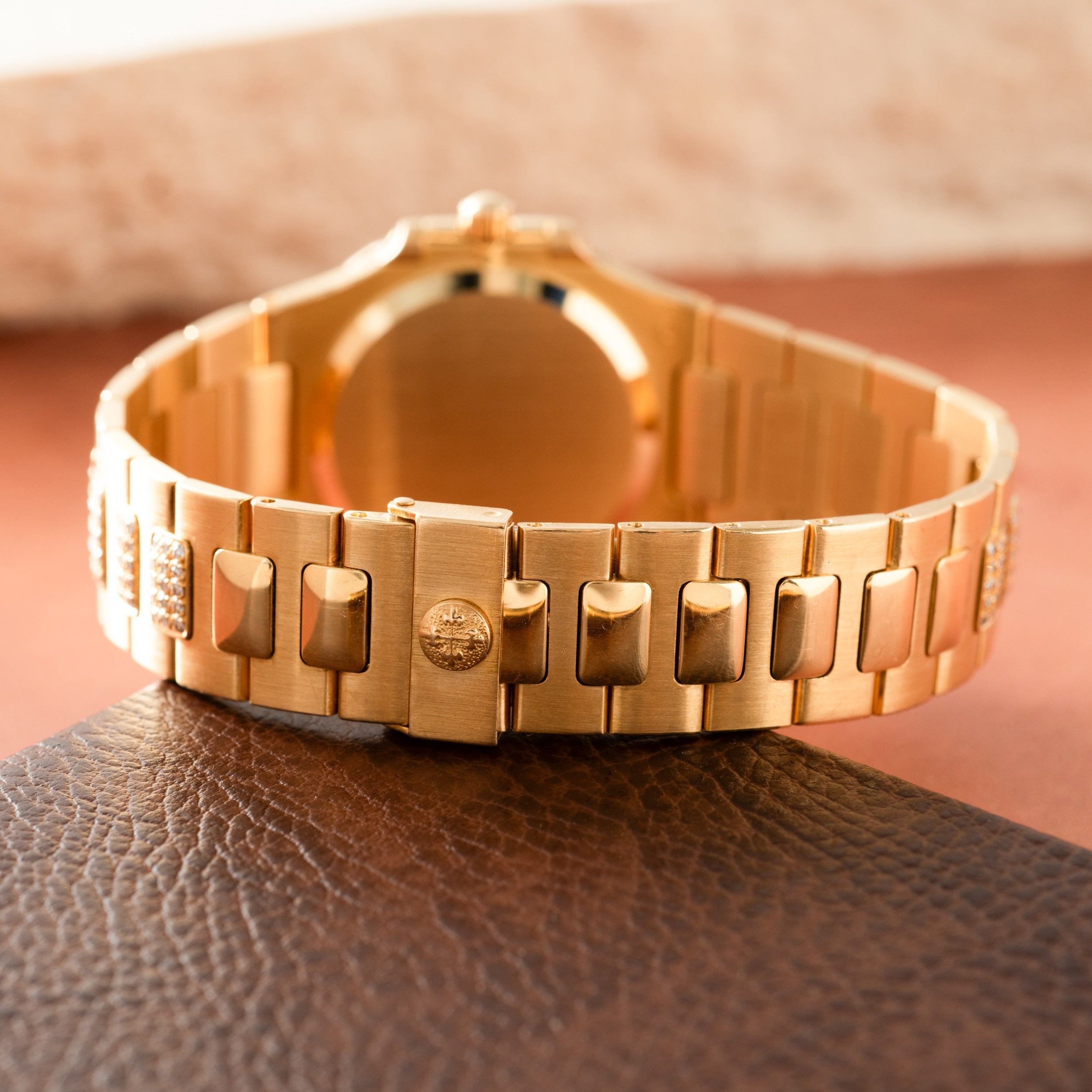 Gold-tone ladies watch with rectangular link bracelet and diamond-set bezel, shown from behind on leather surface.