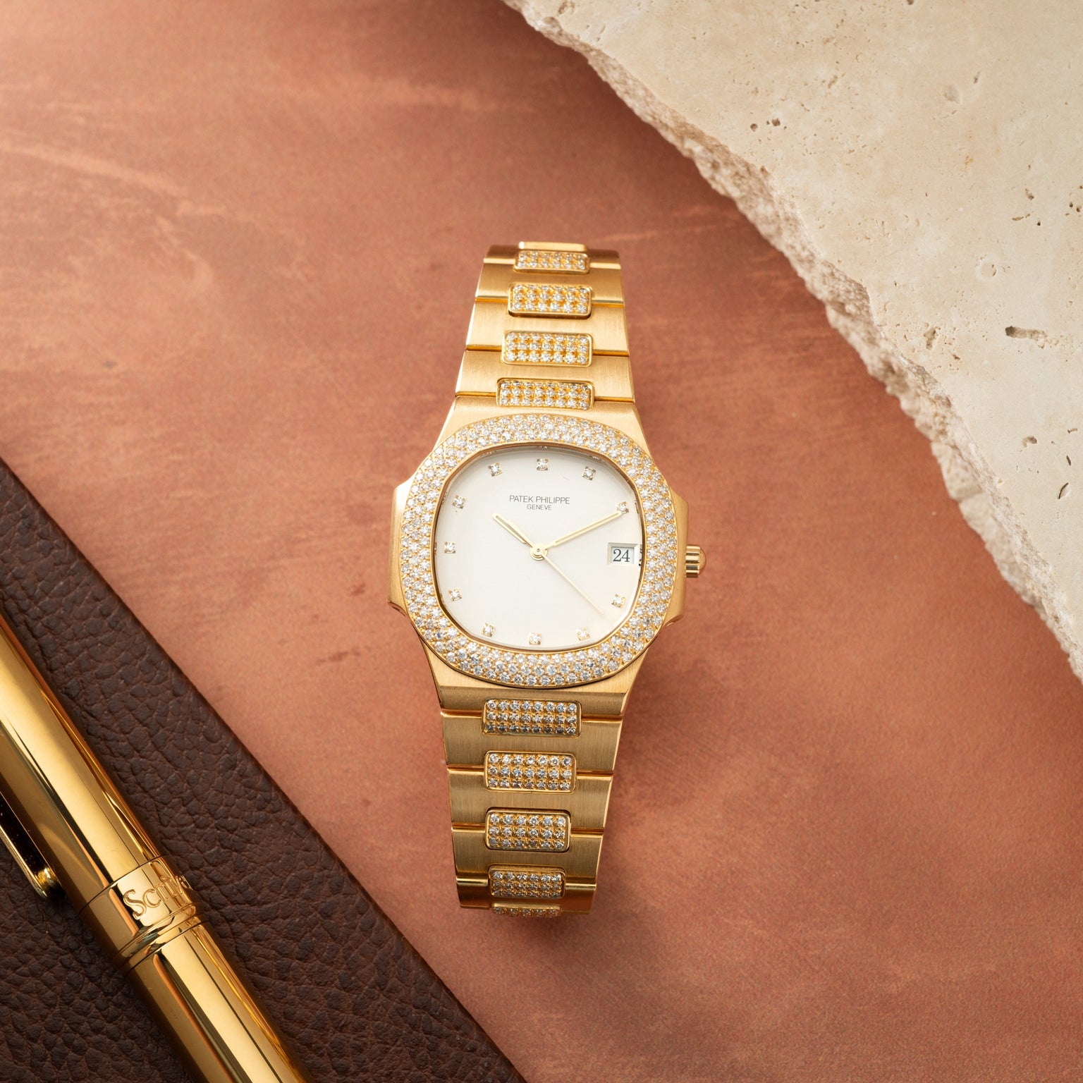 Gold Patek Philippe Nautilus watch with diamond-set bezel, bracelet, and dial on white face with date window.