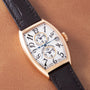 Rose gold tonneau watch with white dial, dual time zones, and black leather strap.