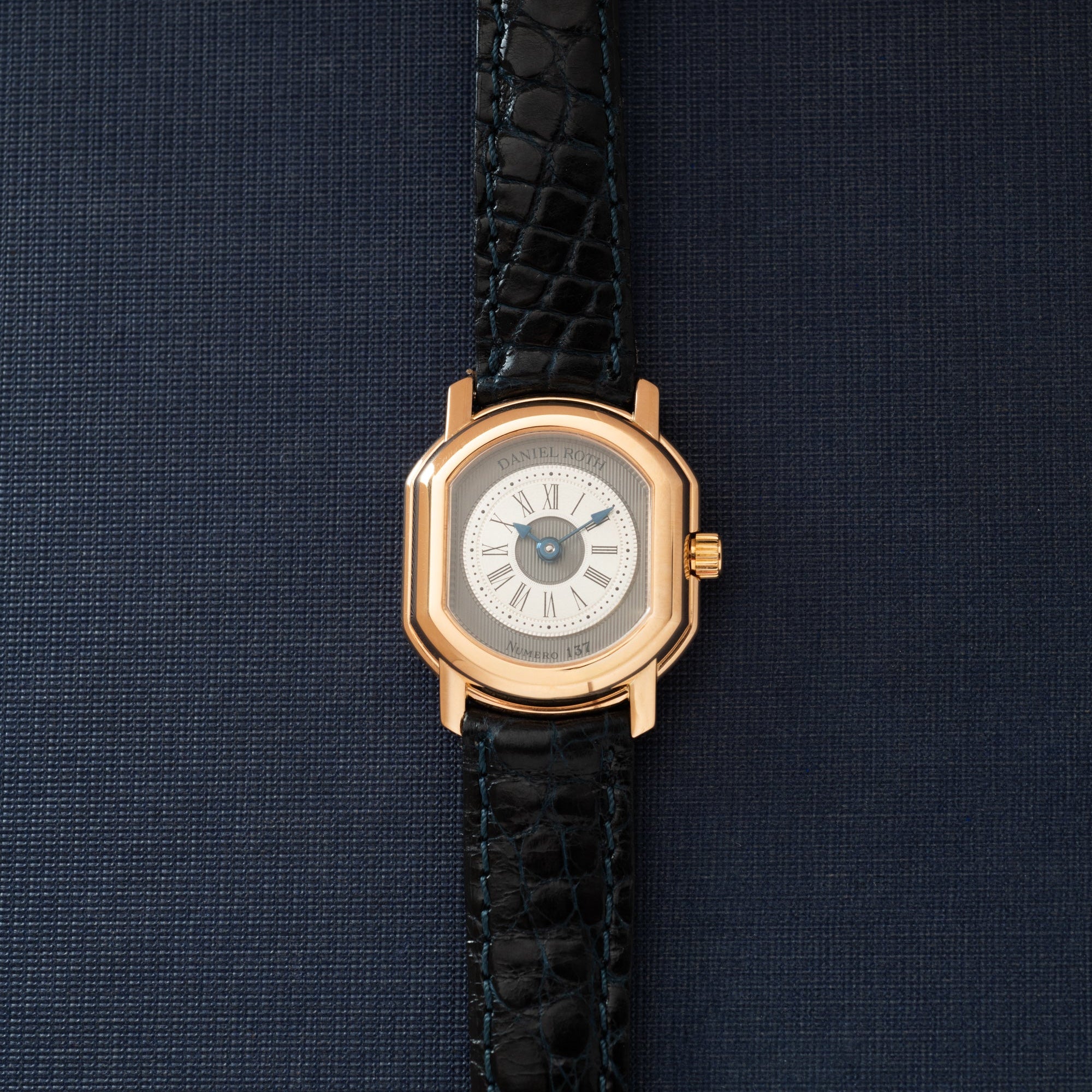 Gold-tone rectangular watch with cream dial, Roman numerals, and black crocodile leather strap.