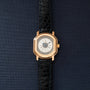 Gold-tone rectangular watch with cream dial, Roman numerals, and black crocodile leather strap.