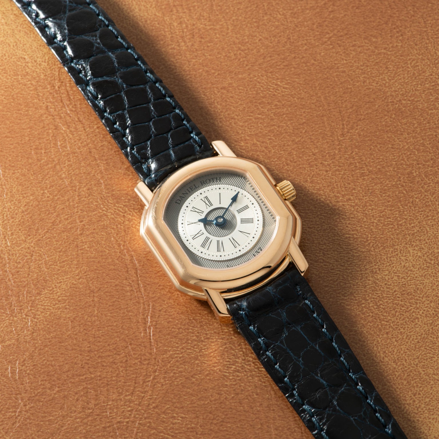 Gold-toned watch with cream dial, Roman numerals, and black crocodile leather strap.