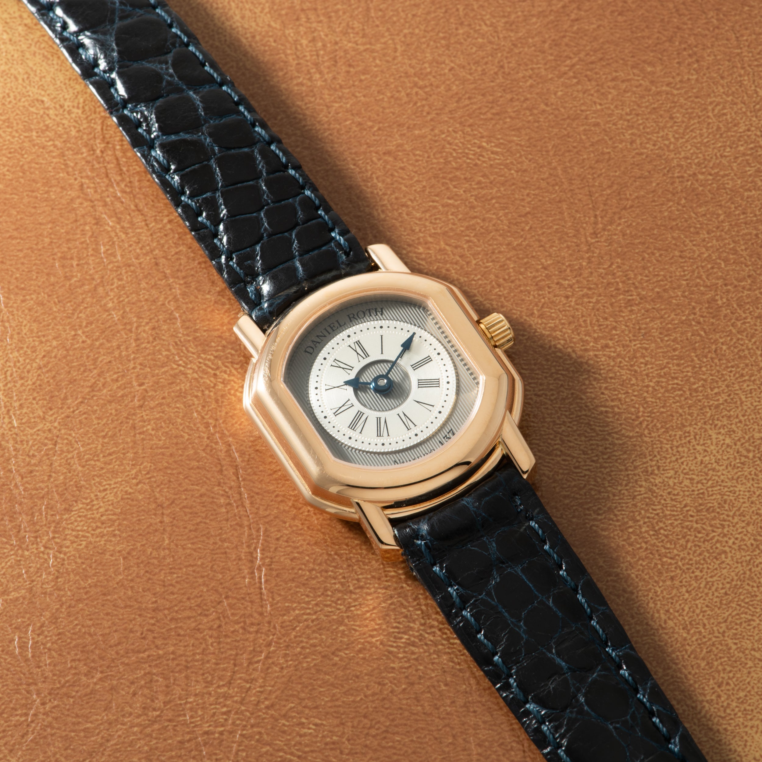 Gold-toned watch with cream dial, Roman numerals, and black crocodile leather strap.