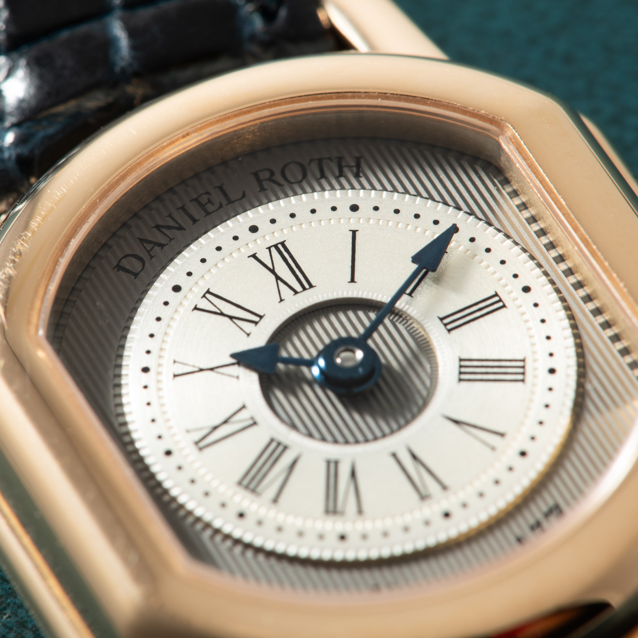 Rose gold watch with cream dial, Roman numerals, blue hands, and "Daniel Roth" text visible on bezel.