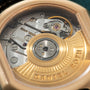 Close-up of automatic watch movement with gold rotor, silver bridges, and Daniel Roth engraving visible.