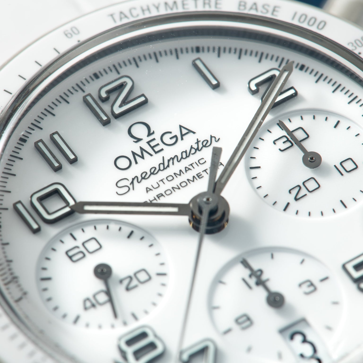 Omega Speedmaster chronograph watch face with white dial, tachymeter bezel, and multiple subdials.