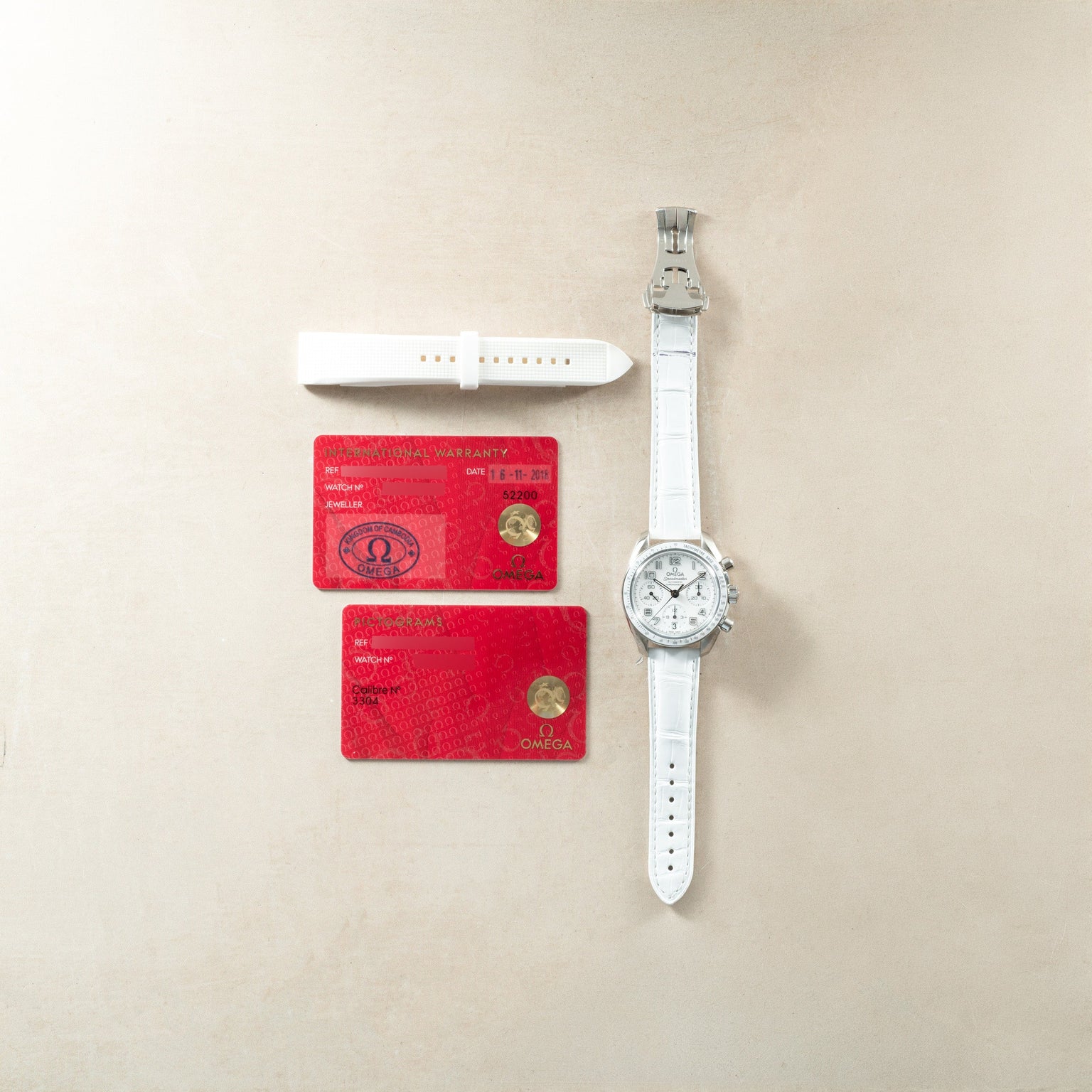 Stainless steel chronograph watch with white dial and leather strap, displayed with white strap and red warranty cards.
