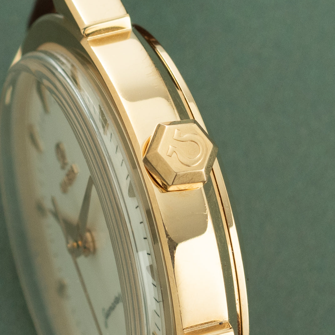 Gold-tone watch with cream leather strap, hexagonal crown marked with "5", and circular dial visible against green background