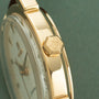 Gold-tone watch with cream leather strap, hexagonal crown marked with "5", and circular dial visible against green background