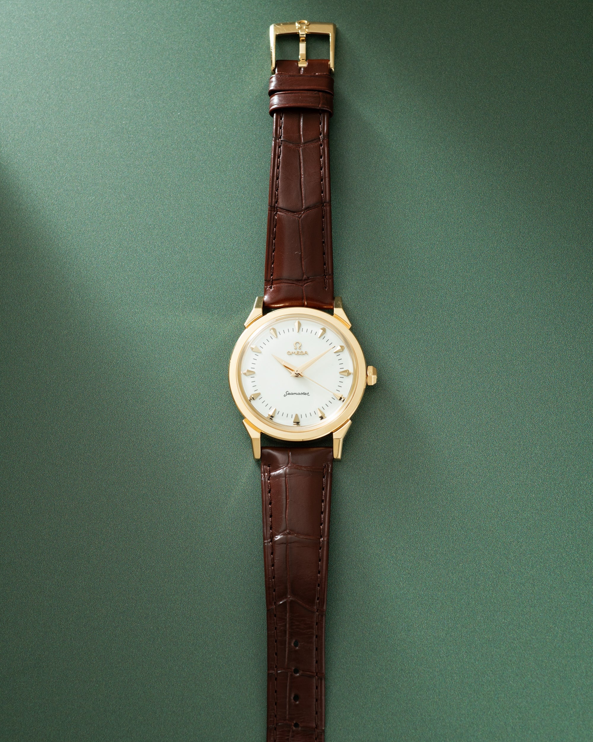 Gold-tone watch with white dial, hour markers, and burgundy crocodile-embossed leather strap with gold buckle.
