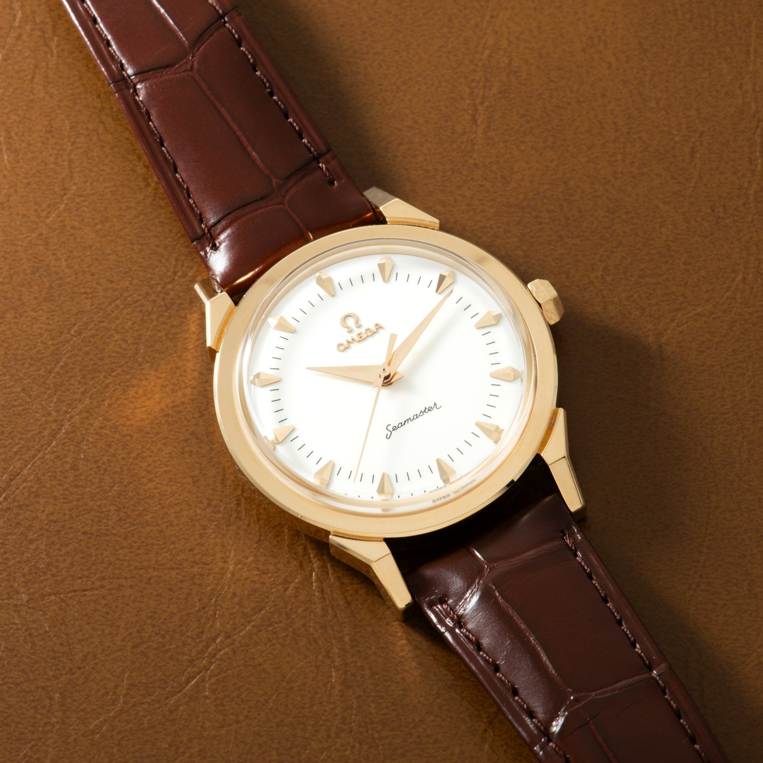 Gold-tone watch with white dial, applied hour markers, and dark burgundy crocodile-embossed leather strap.