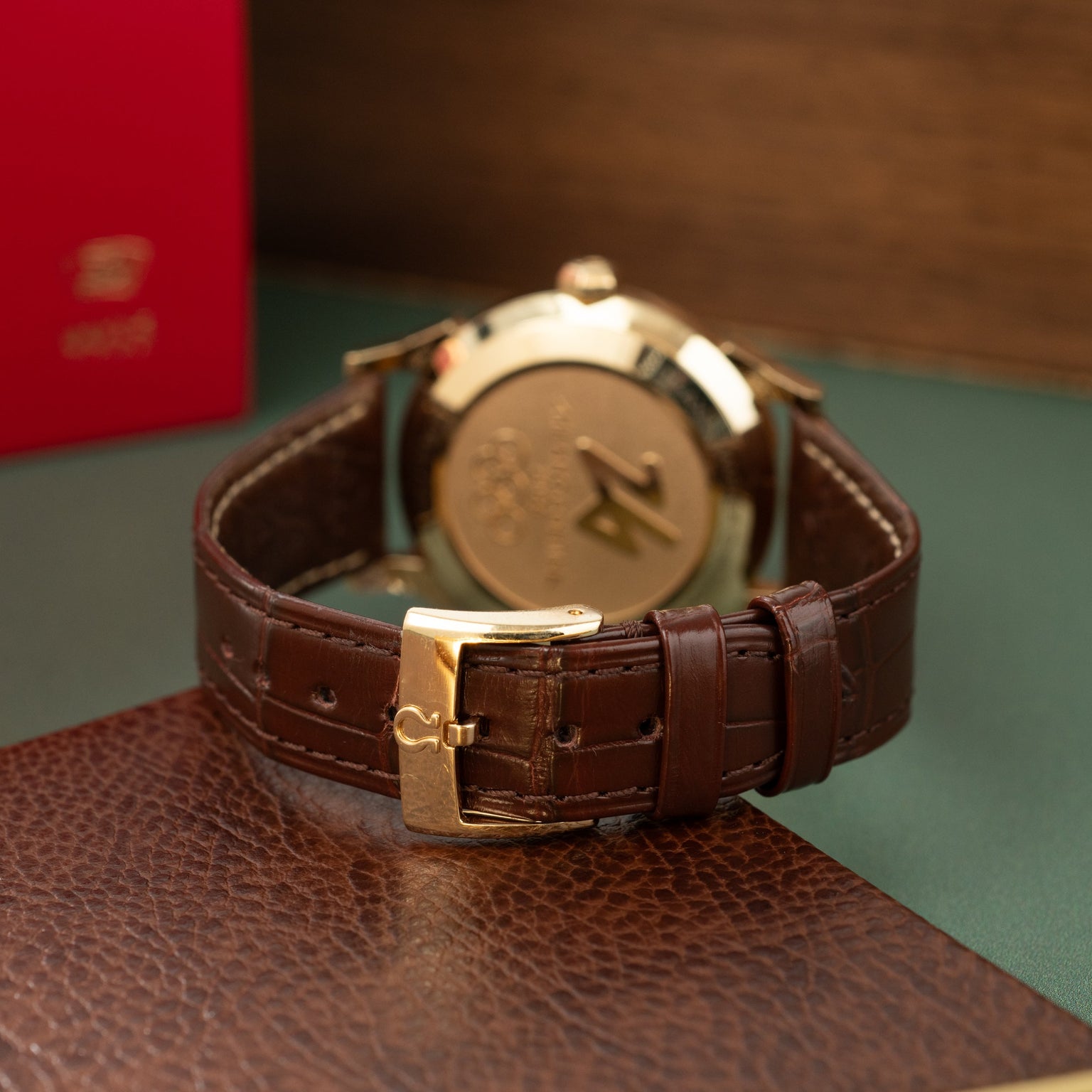 Omega Milano Cortina watch with bronze dial, gold-tone case, and brown leather crocodile-embossed strap with gold buckle.