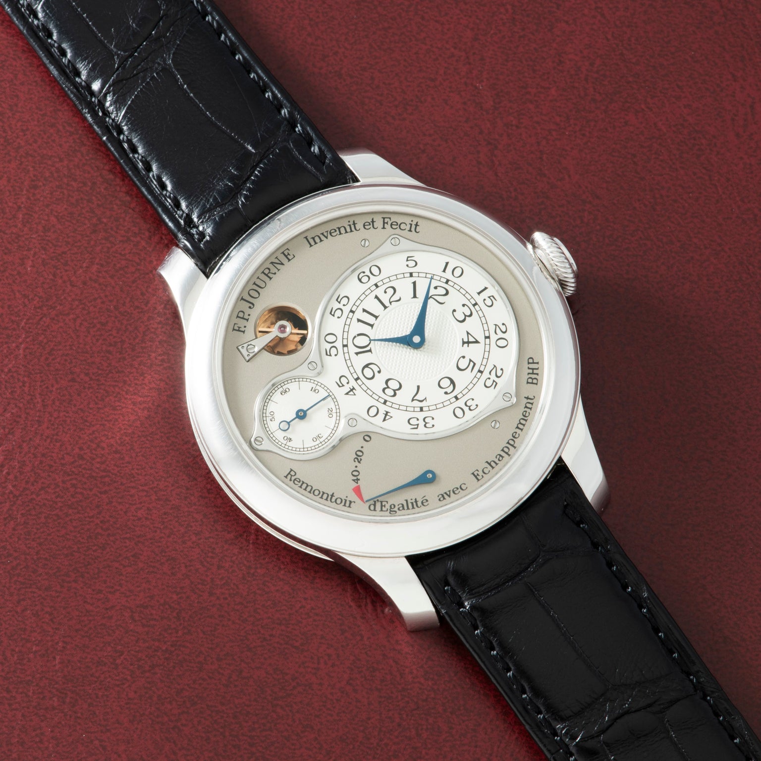 Luxury chronometer watch with silver case, cream dial, blue hands, and black crocodile leather strap on burgundy background.