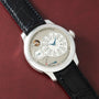 Luxury chronometer watch with silver case, cream dial, blue hands, and black crocodile leather strap on burgundy background.