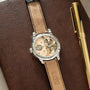 Stainless steel watch with skeleton dial showing exposed movement, tan leather strap with contrasting stitching, displayed on