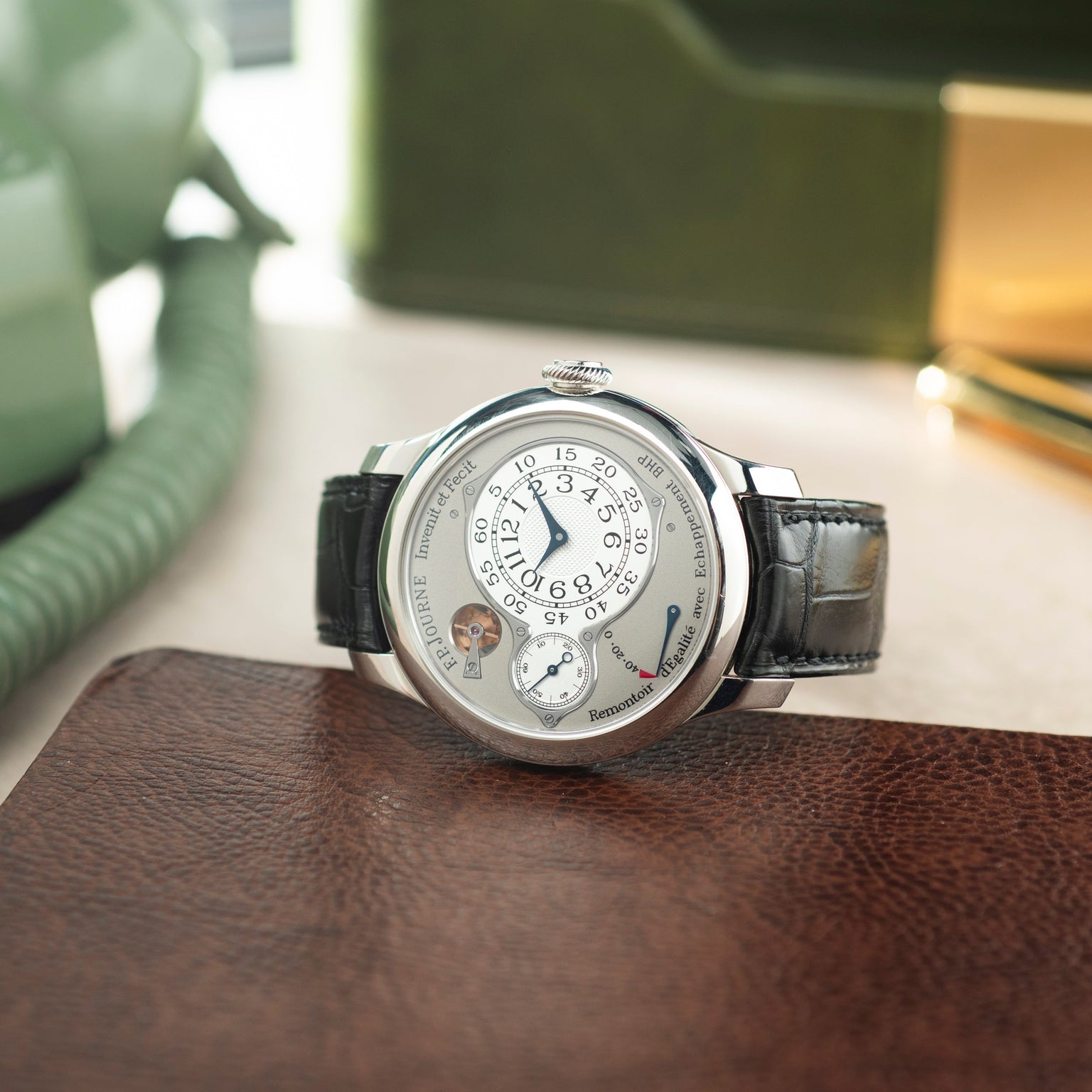 Silver-toned round watch with white dial, circular time display, black leather strap, displayed on brown leather surface.